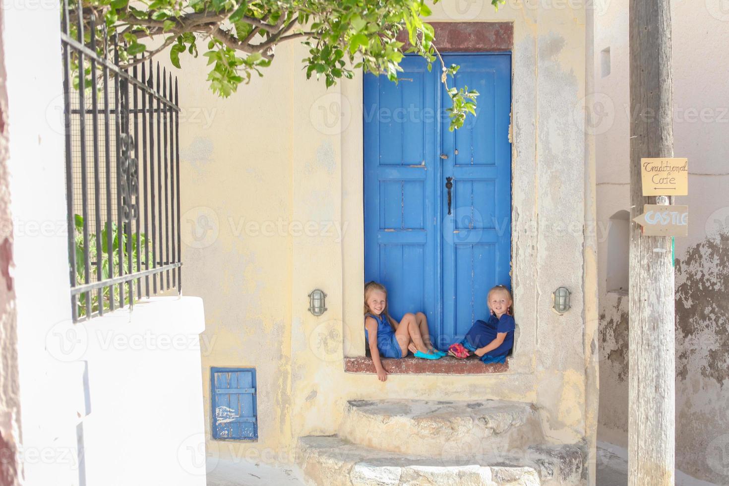 Two little adorable girls sitting on doorstep of old house in Emporio village, Santorini, Greece photo