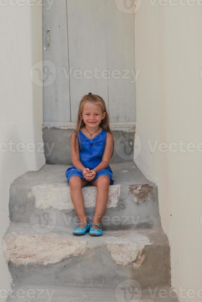 linda niña sentada en la puerta de la casa antigua en el pueblo de emporio, santorini, grecia foto