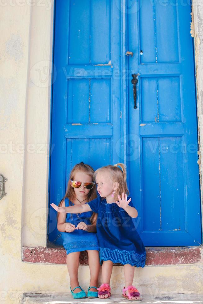 Little adorable girls sitting near old blue door in Greek village of Emporio, Santorini photo