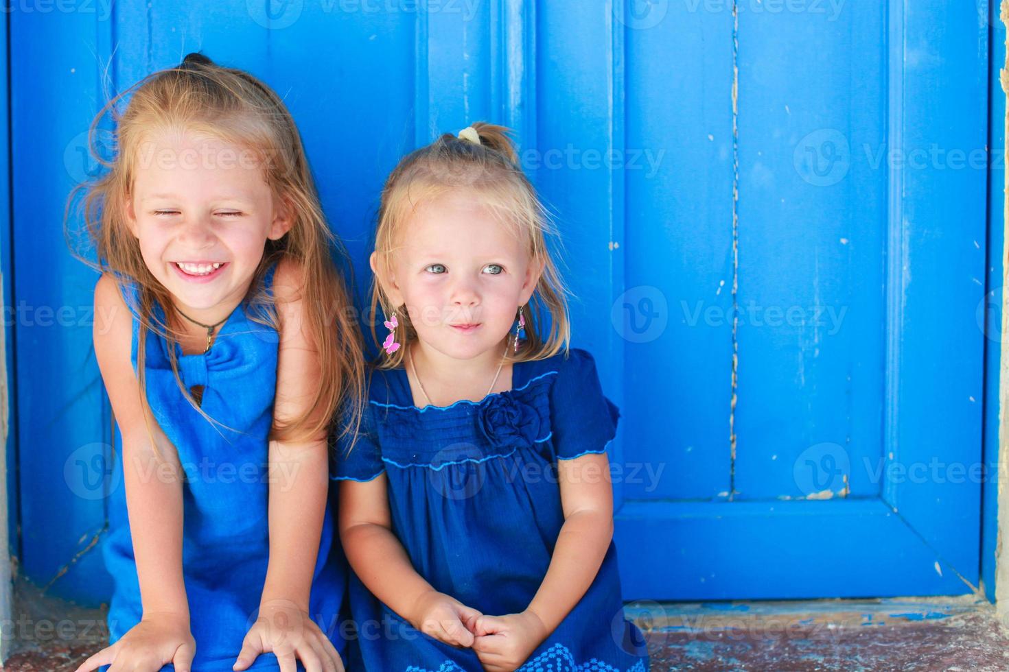 Closeup of Little adorable girls sitting near old blue door in Greek village, Emporio, Santorini photo