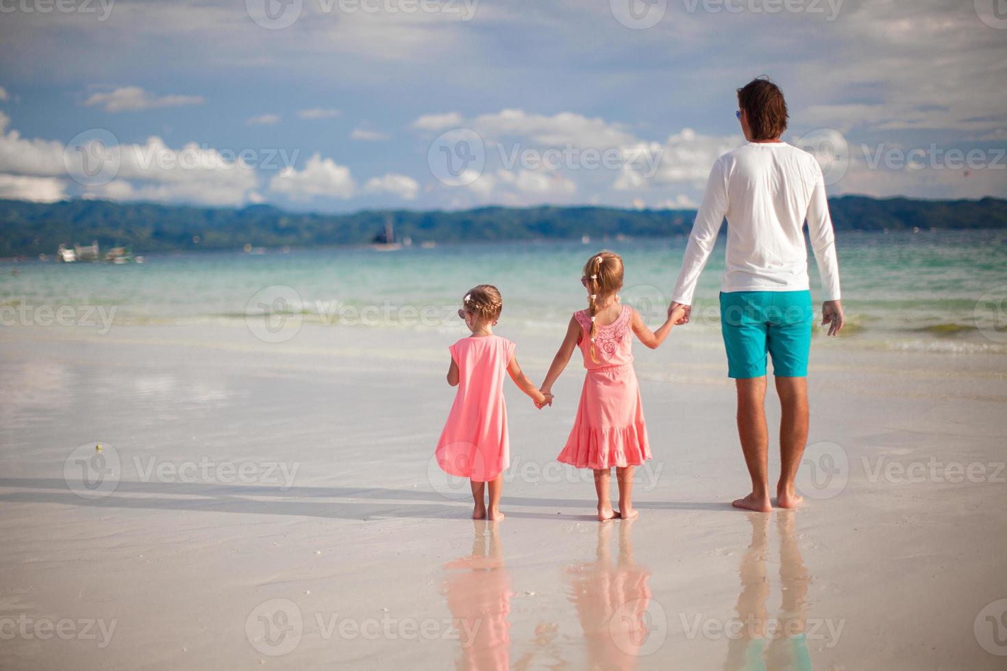 vista trasera del padre y sus dos hijas pequeñas caminando junto al mar foto