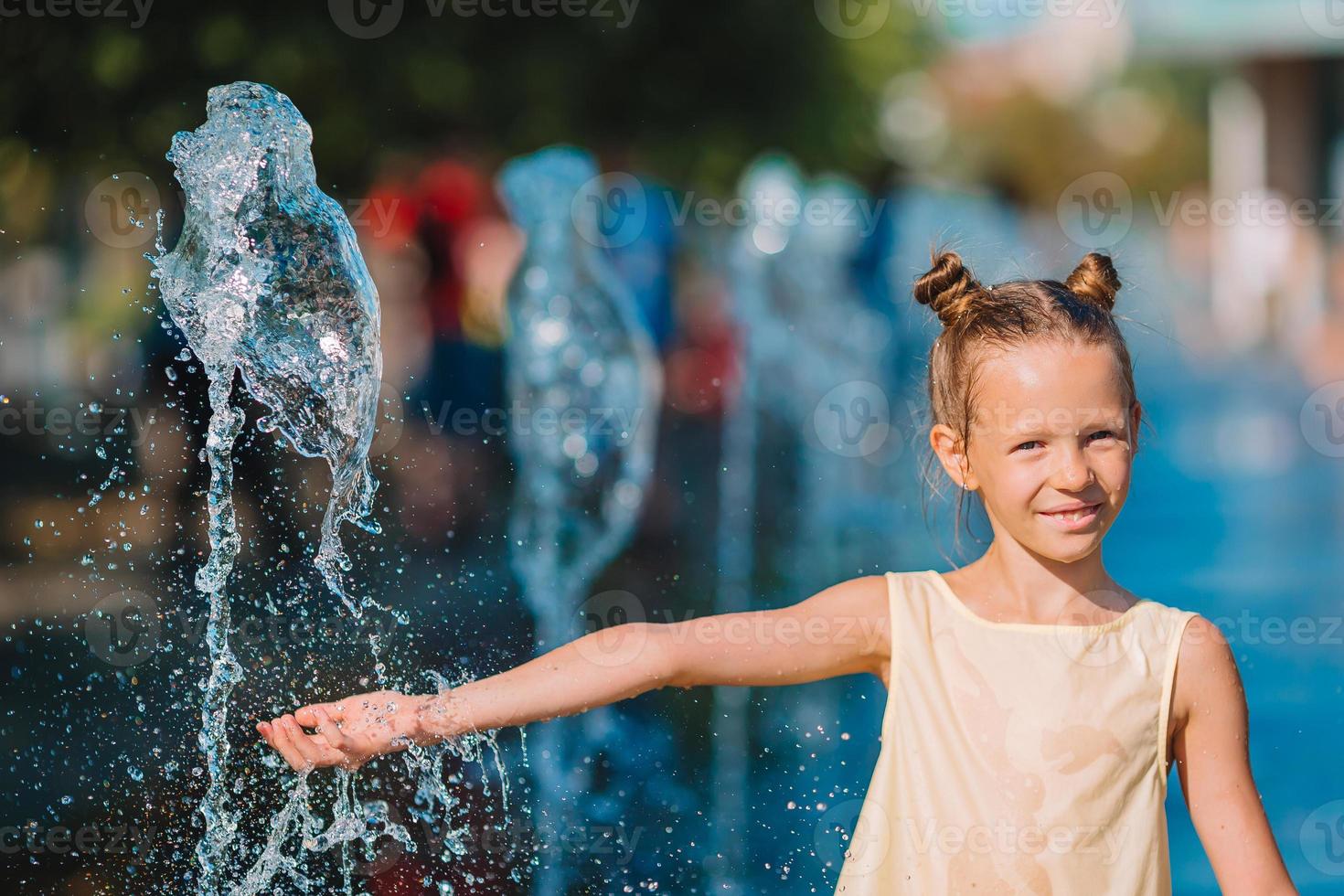 Little adorable girl have fun in street fountain at hot sunny day photo