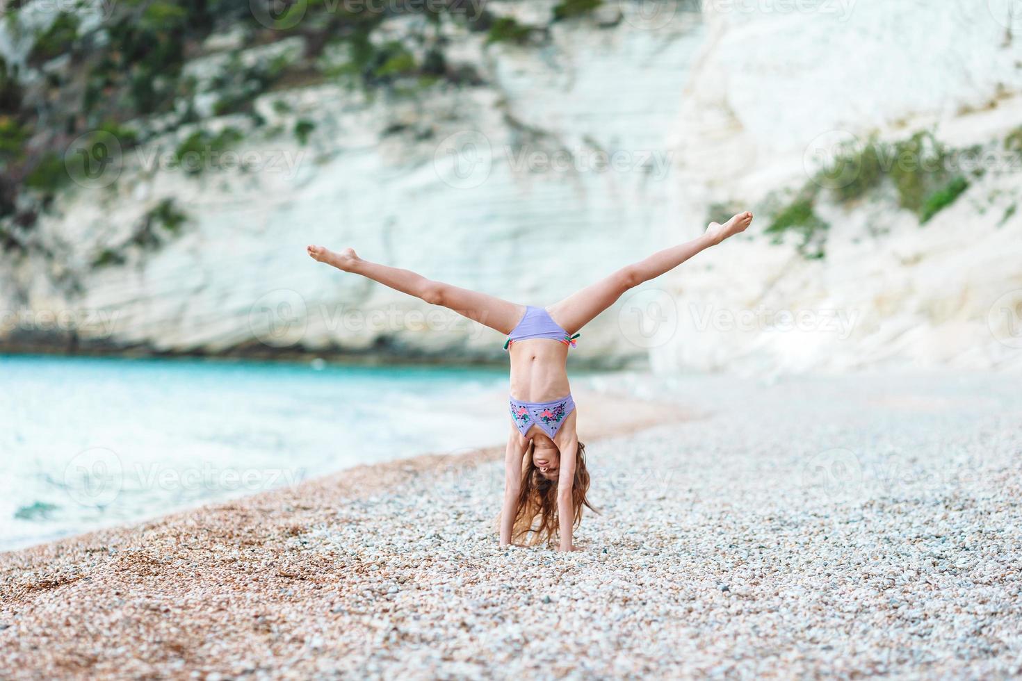 Active little girl at beach having a lot of fun. Cute kid making sporty exercises on the seashore photo