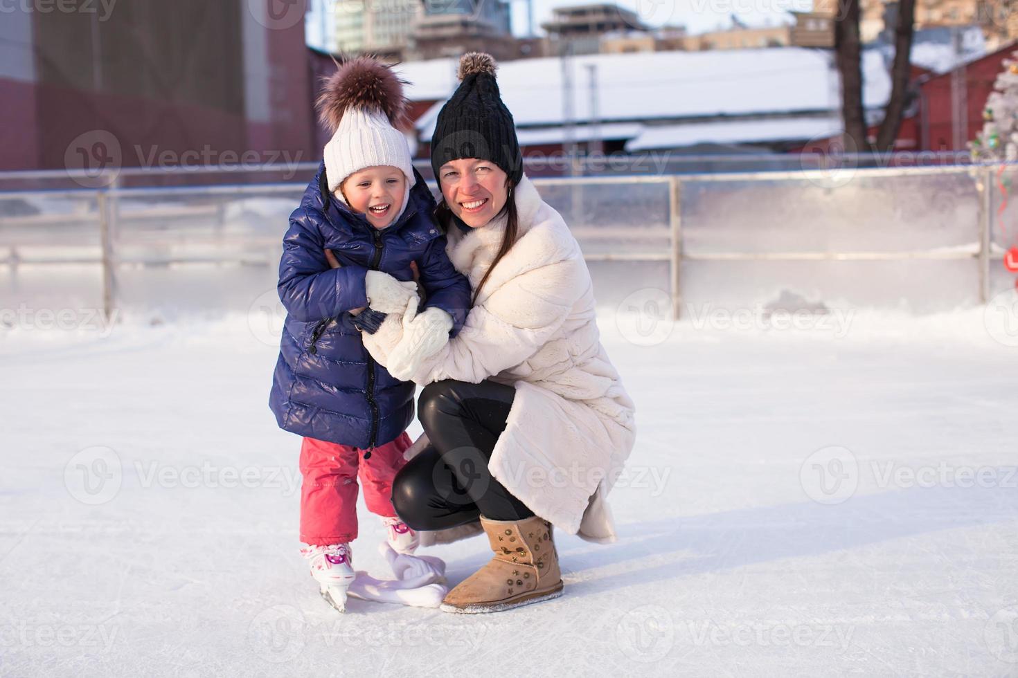 sonriente joven madre y su linda hijita patinando sobre hielo juntos foto
