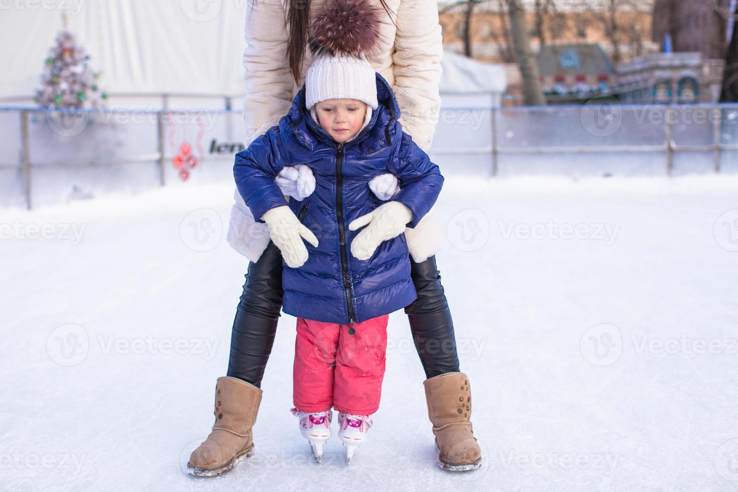 feliz adorable niña y joven madre aprendiendo patinaje sobre hielo foto