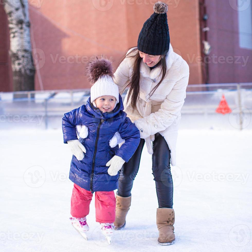 Happy excited little girl and her young mother learning ice-skating photo