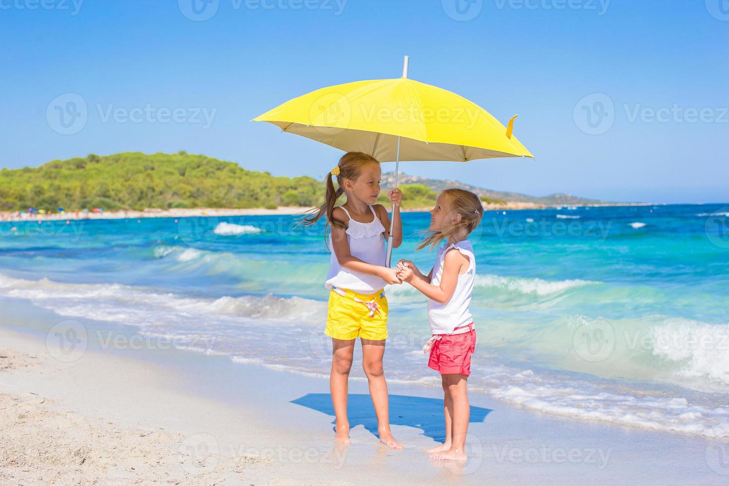 Little girls with big yellow umbrella walking on tropical beach photo