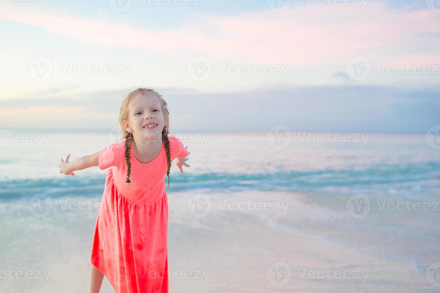 Adorable little girl at beach having a lot of fun in the evening. Happy kid looking at camera background beautiful sky and sea photo