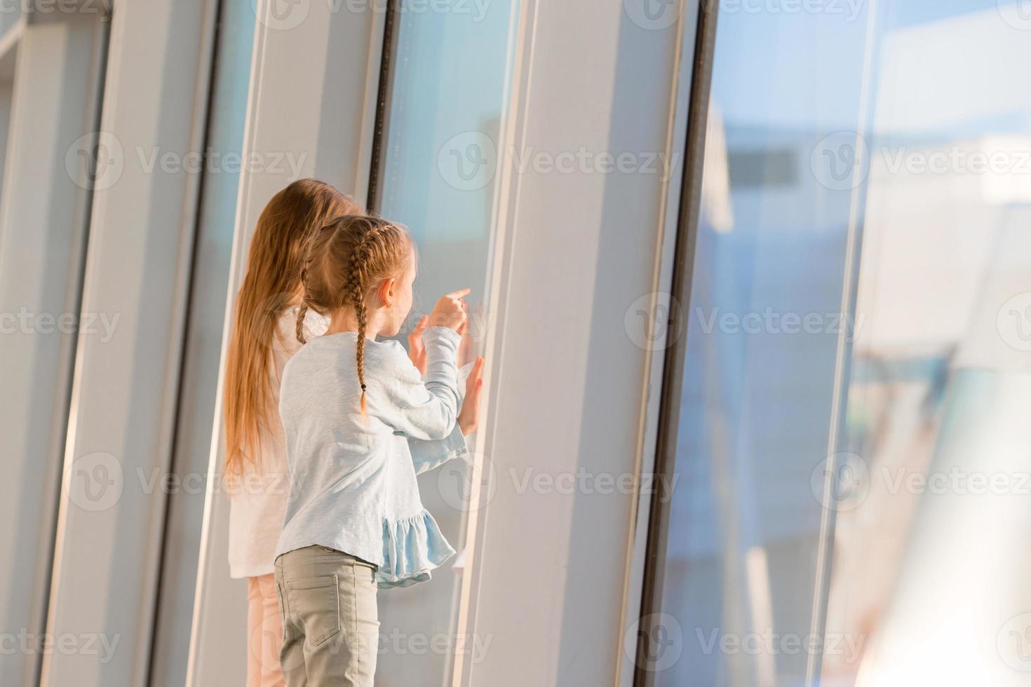 Little kids together in airport waiting for boarding near big window photo