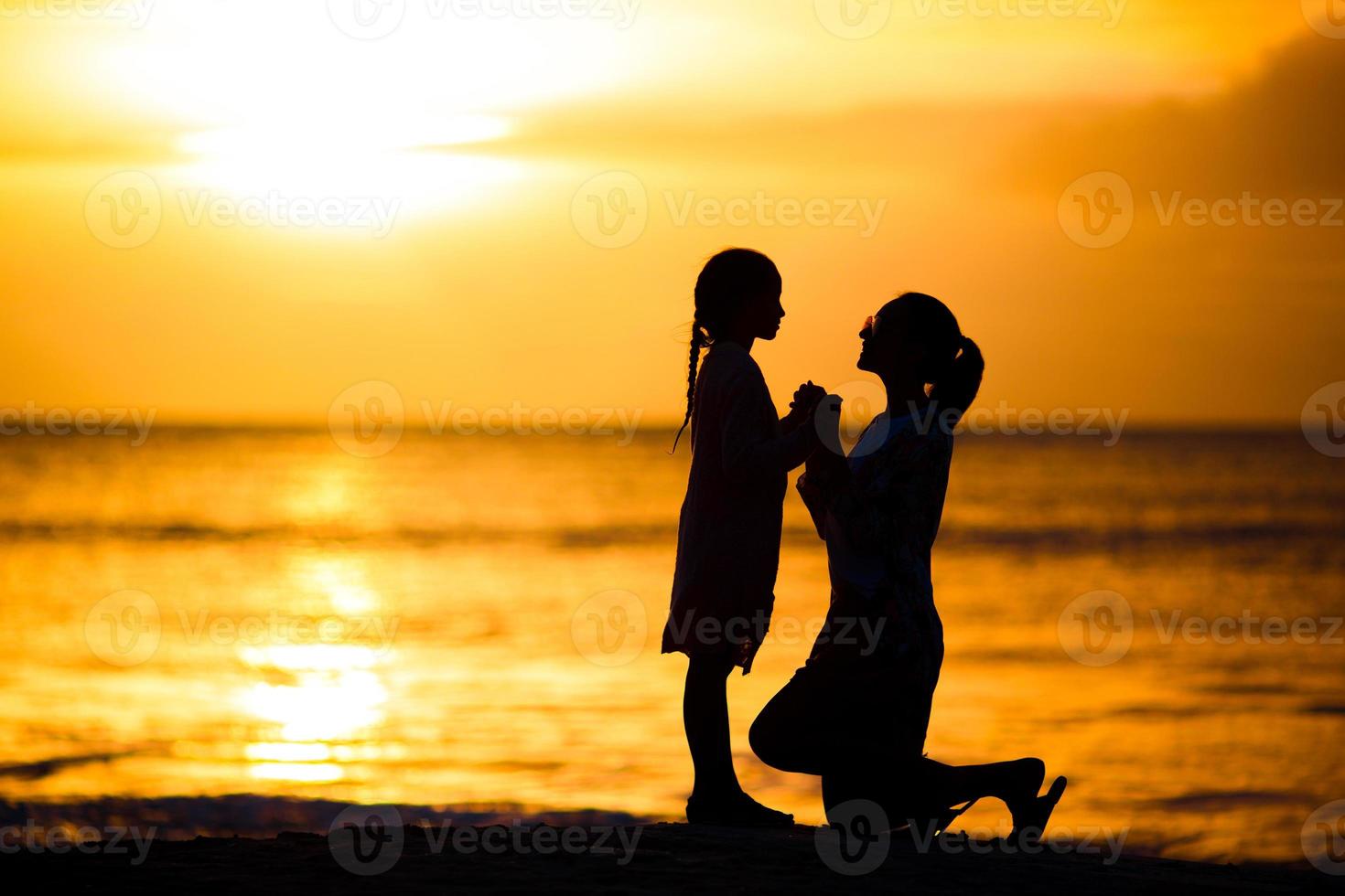 Little girl and happy mother silhouette in the sunset at the beach photo