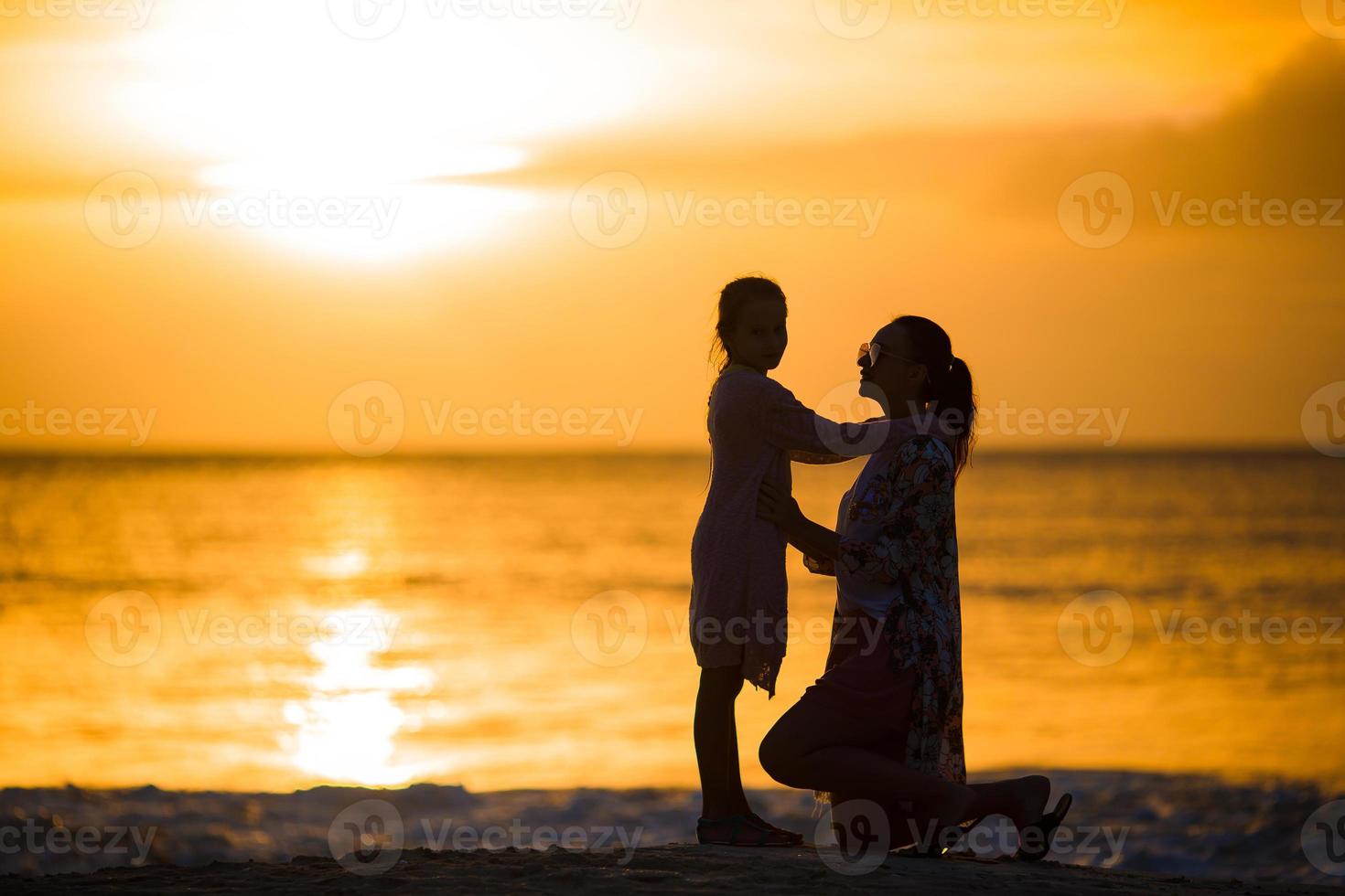 silueta de niña y madre feliz al atardecer en la playa foto