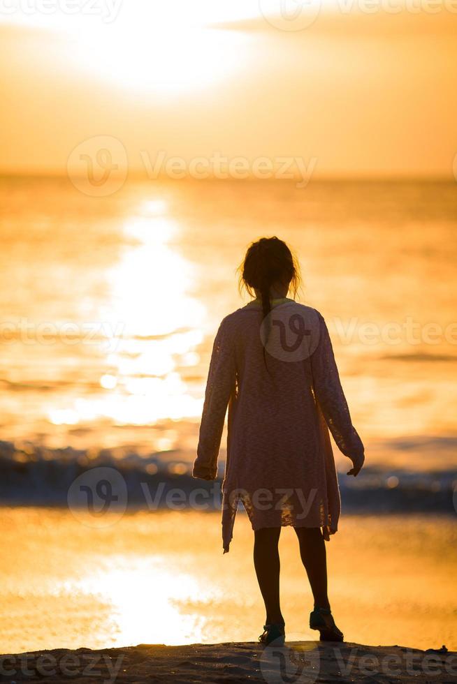 Adorable happy little girl walking on white beach at sunset. photo