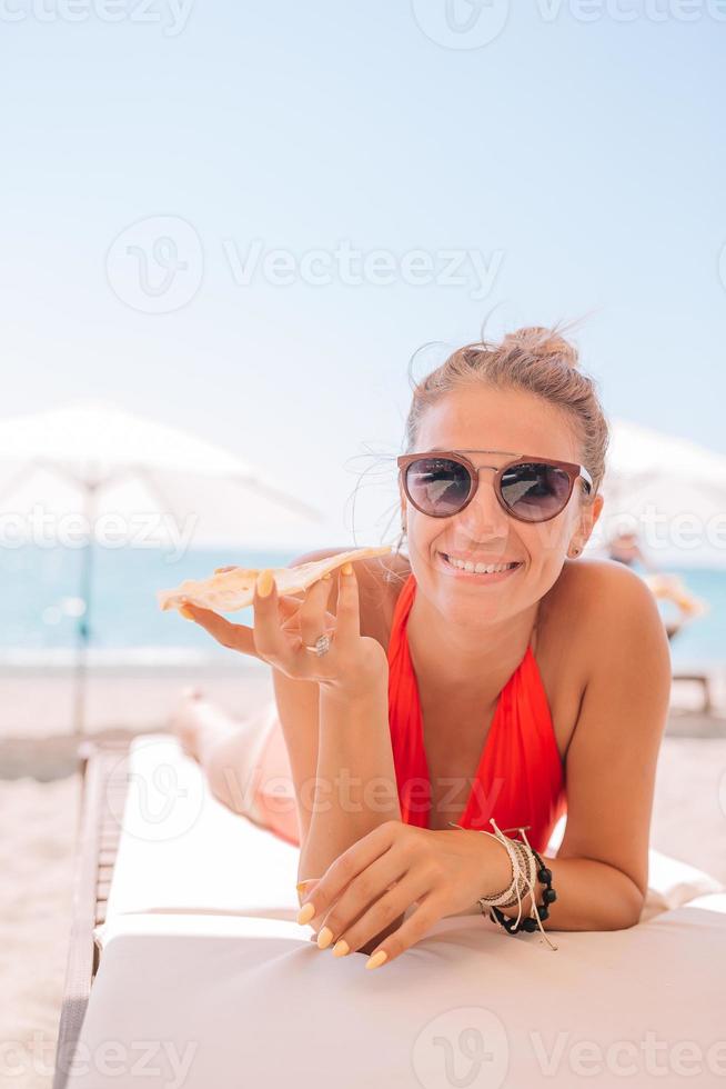 Young woman in swimsuit with cocktail glass on white beach sitting on sunbed photo