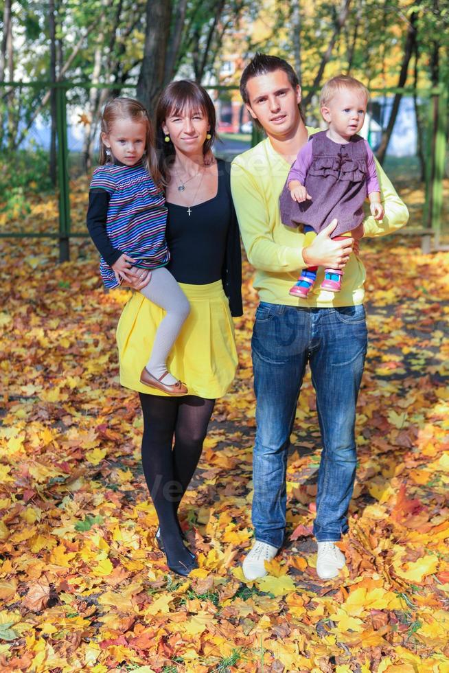 Young charming family of four walking in yellow autumn park photo