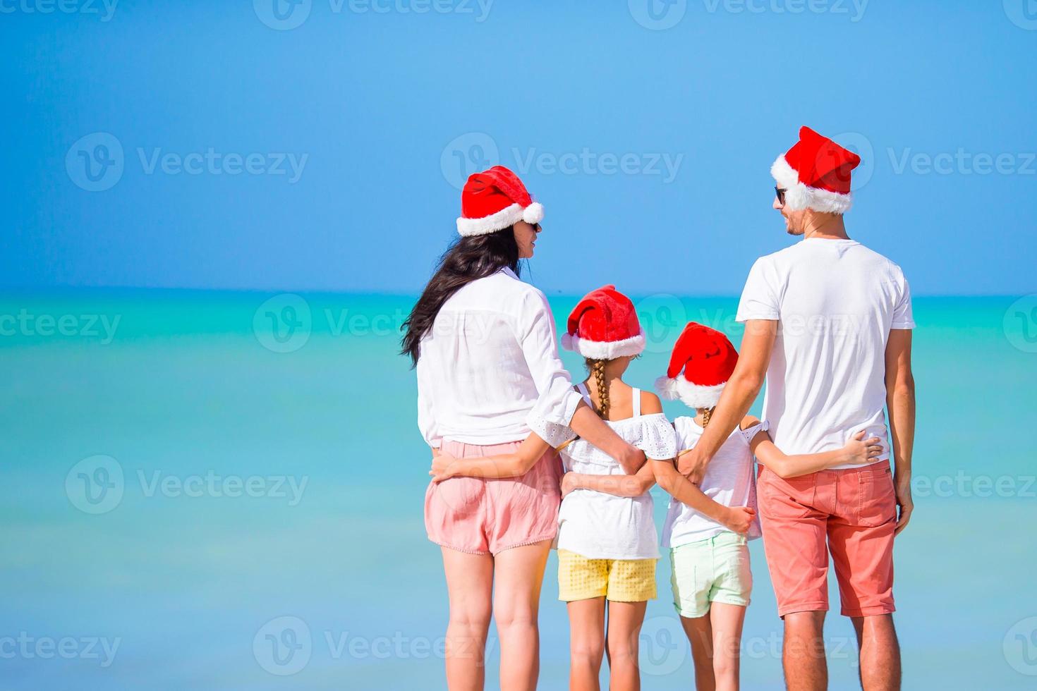 Happy family in red Santa hats on a tropical beach celebrating Christmas vacation photo