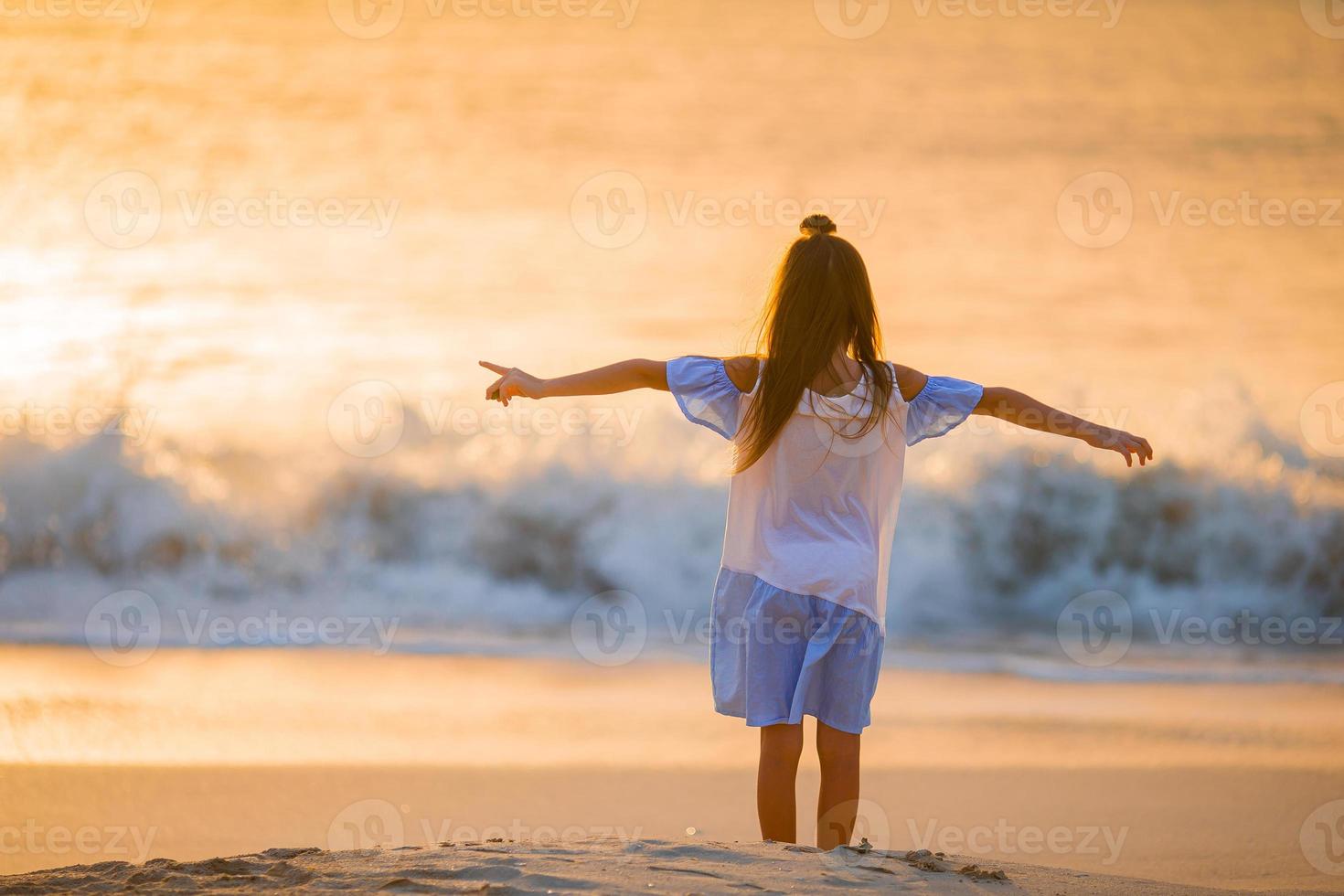 adorable niña feliz caminando en la playa blanca al atardecer. foto