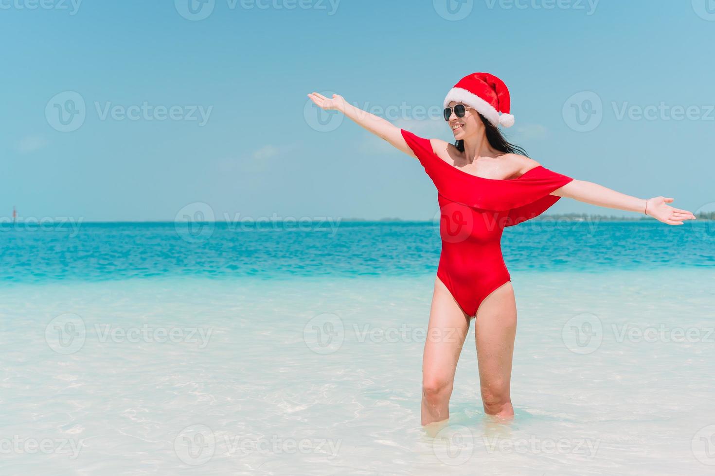 Young woman in Santa Hat walking spread her hands on white sandy beach photo