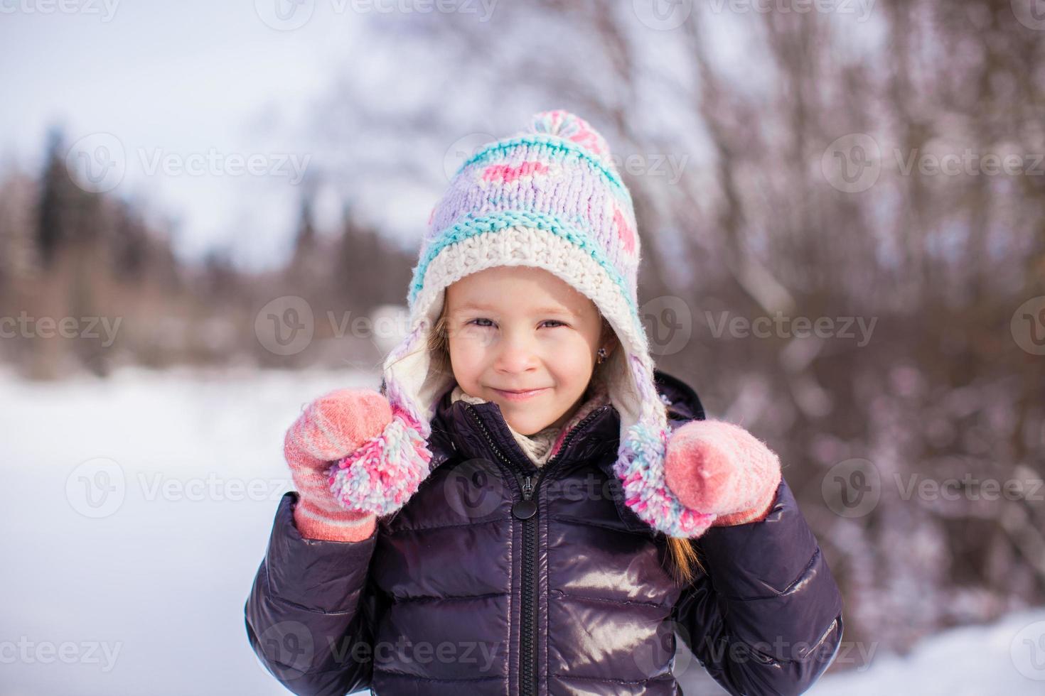 Portrait of little adorable girl in winter hat at snowy forest photo