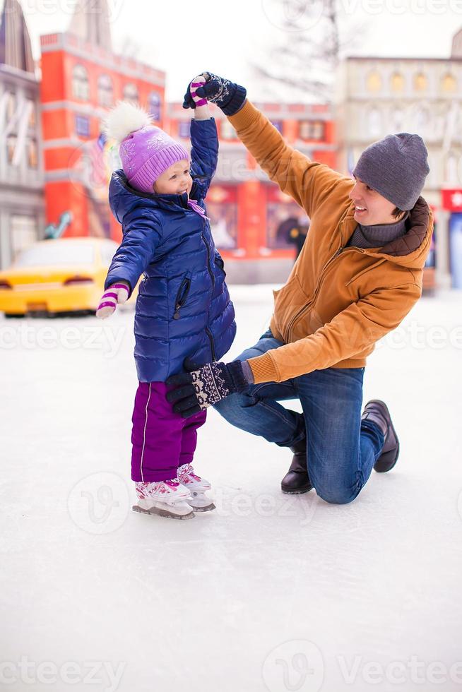 Little happy girl with young father have fun on skating rink photo