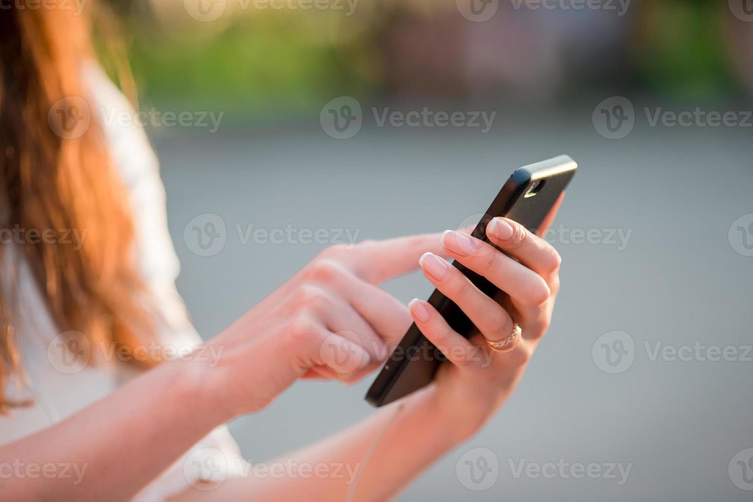 Closeup of female hands is holding cellphone outdoors on the street in evening lights. Woman using mobile smartphone. photo