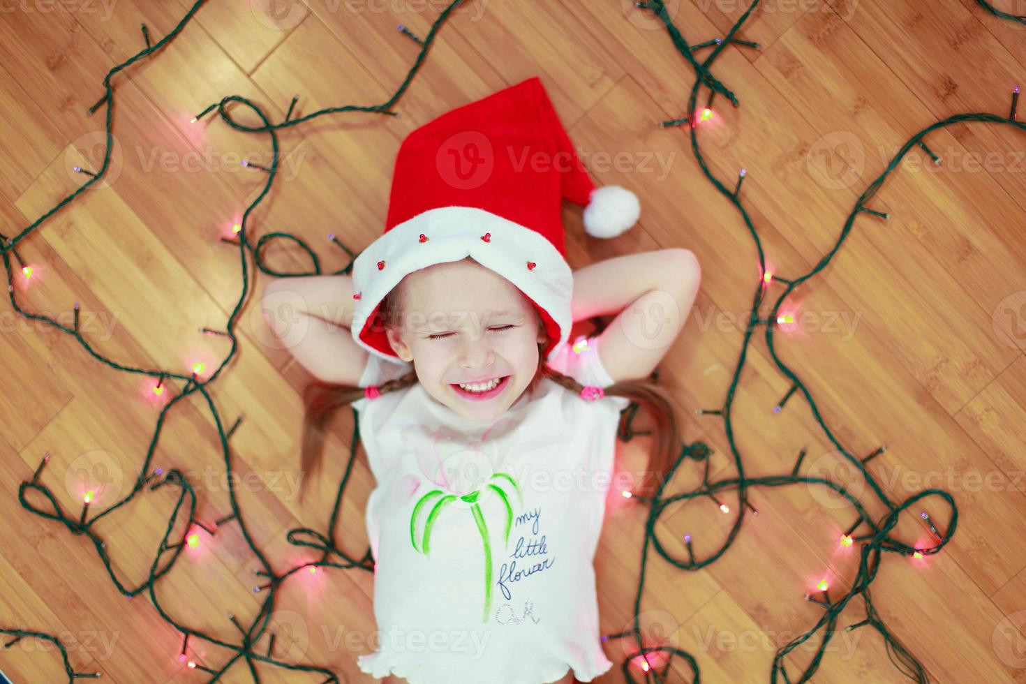 Little happy girl lies among the multi-colored lights on a wooden floor photo