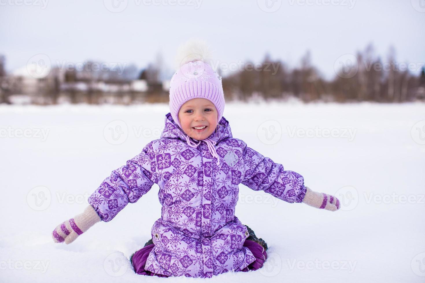 Little adorable girl sitting on the snow at winter sunny day photo