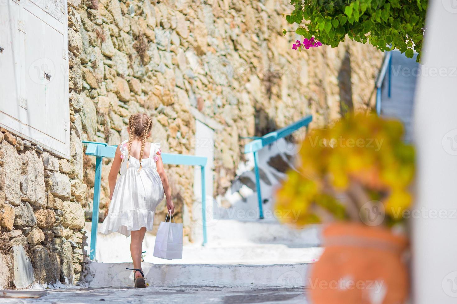 Adorable girl outdoors in greek village. Kid at street of typical greek traditional village with white stairs on greek island photo