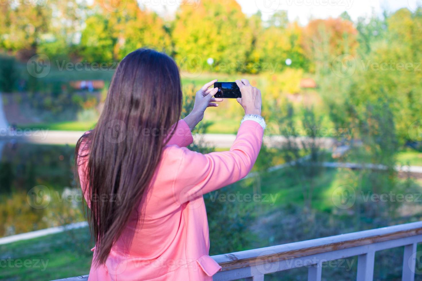 Young woman take a photo by her phone at autumn day
