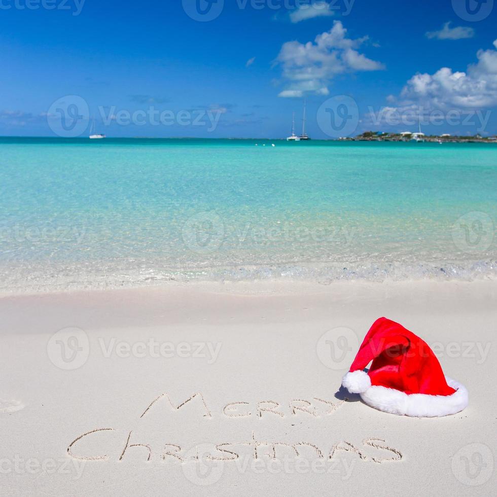 feliz navidad escrita en una playa tropical de arena blanca con sombrero de navidad foto
