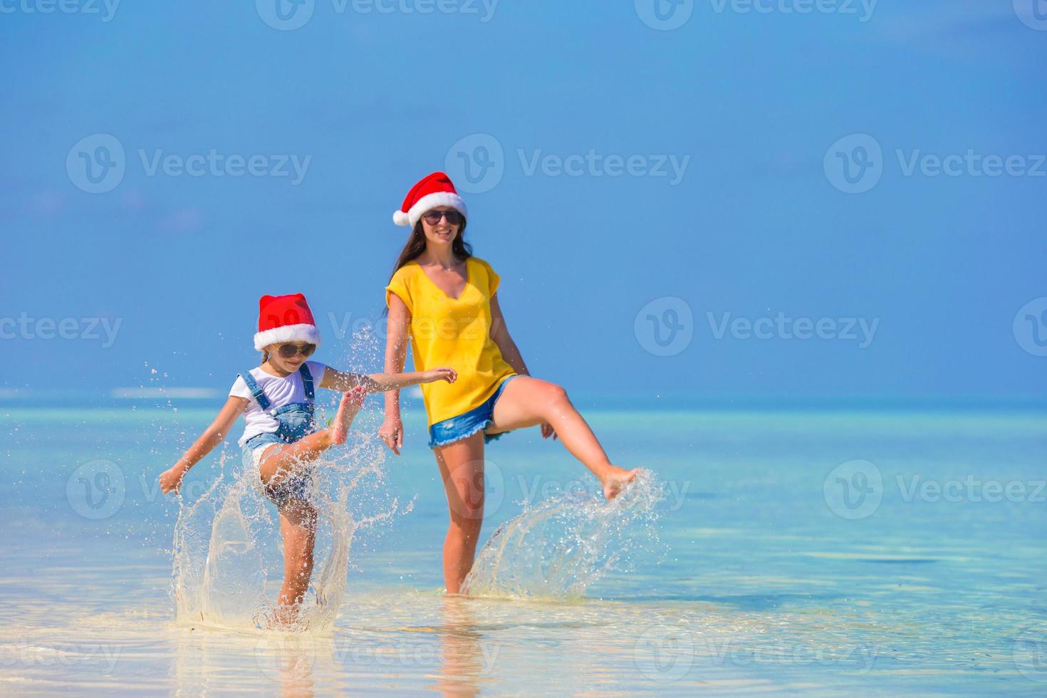 niña y madre joven con sombrero de santa durante las vacaciones en la playa foto