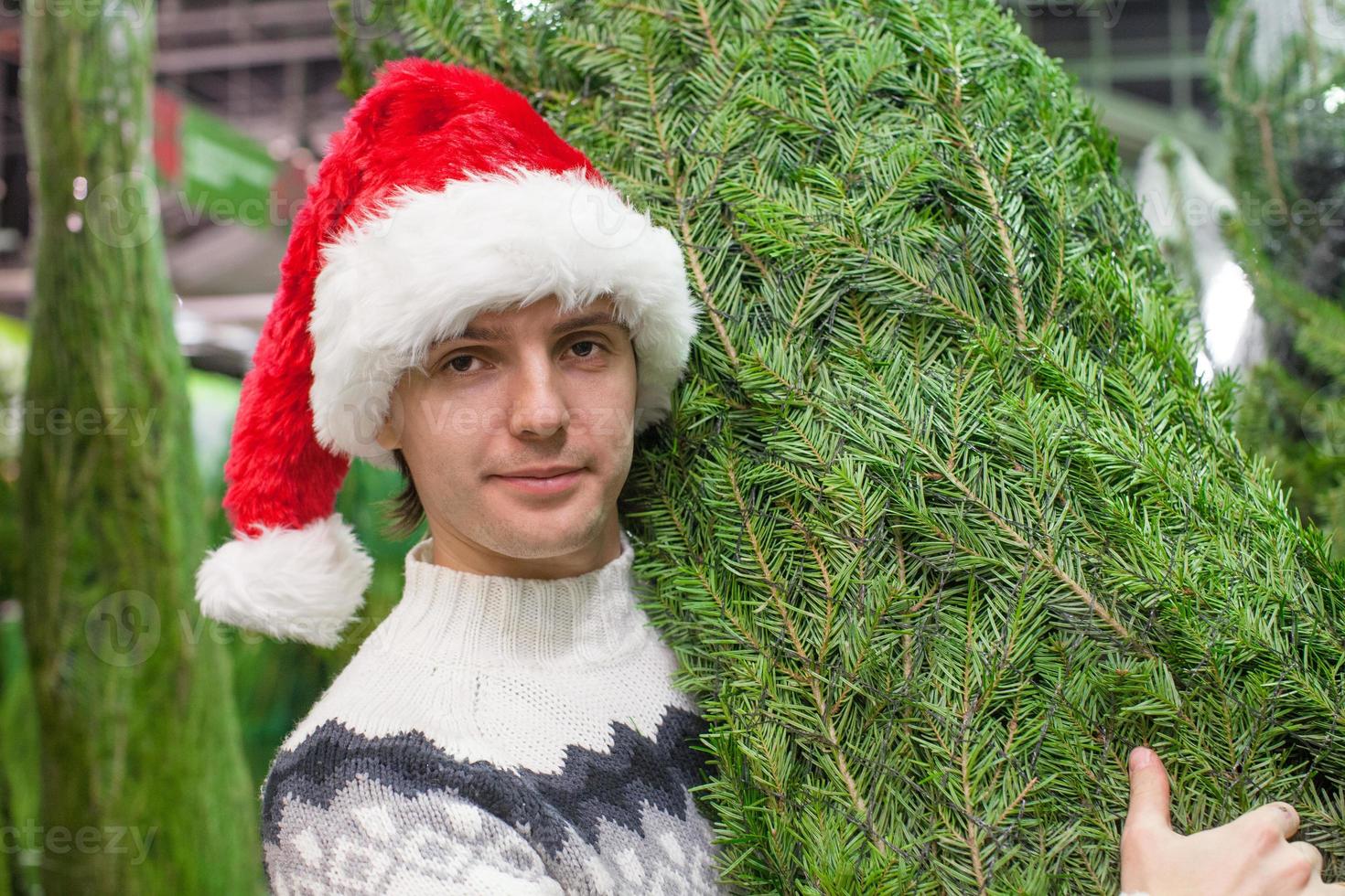 padre joven con sombrero de santa comprando árbol de navidad foto