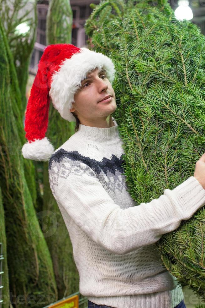 joven con sombrero de santa comprando un árbol de navidad foto