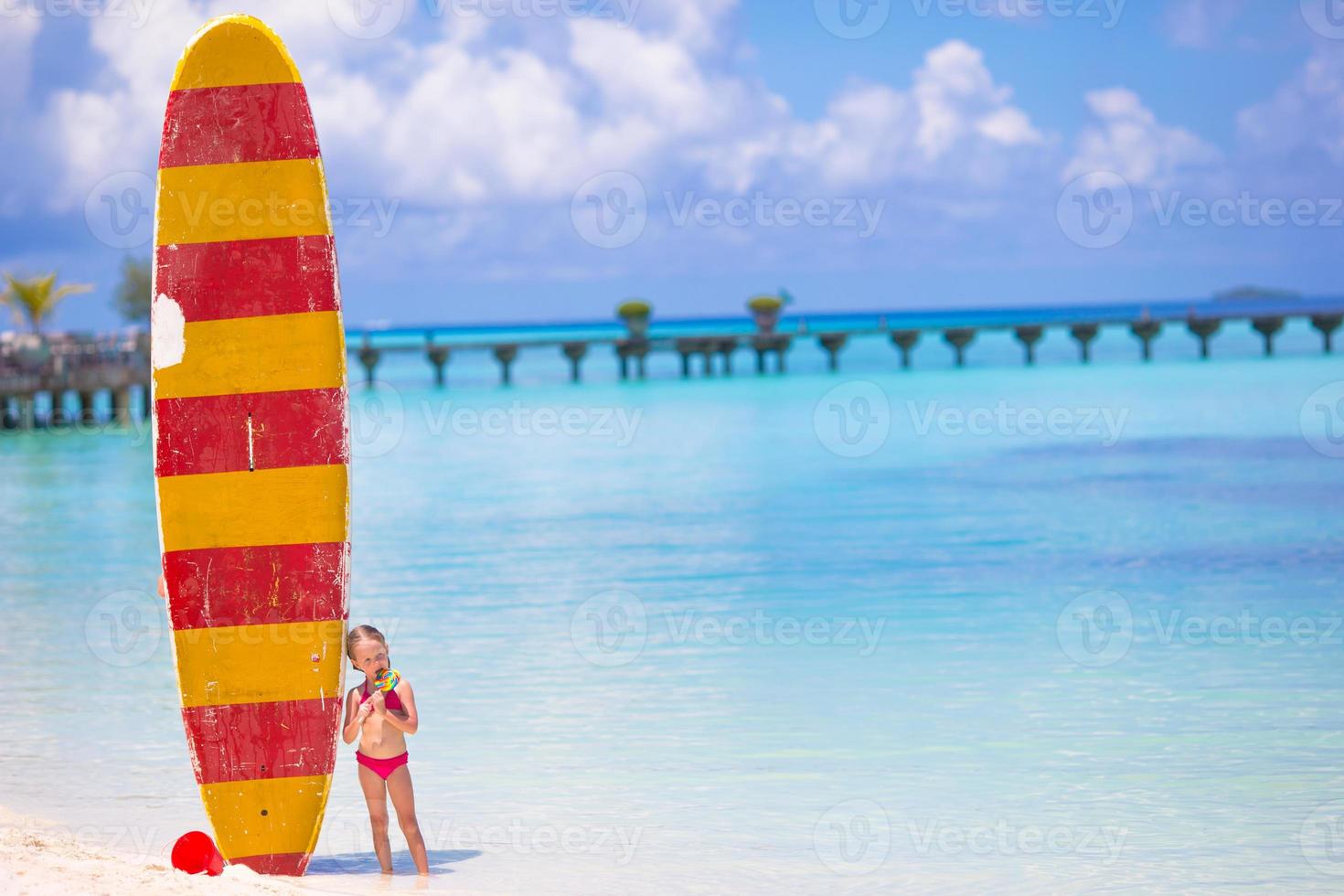 Adorable little girl with big surfboard during tropical vacation photo