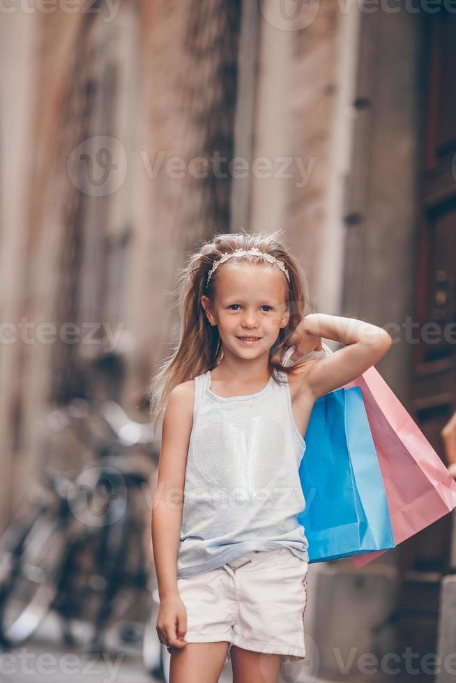 Portrait of adorable little girl walking with shopping bags outdoors in european city. photo