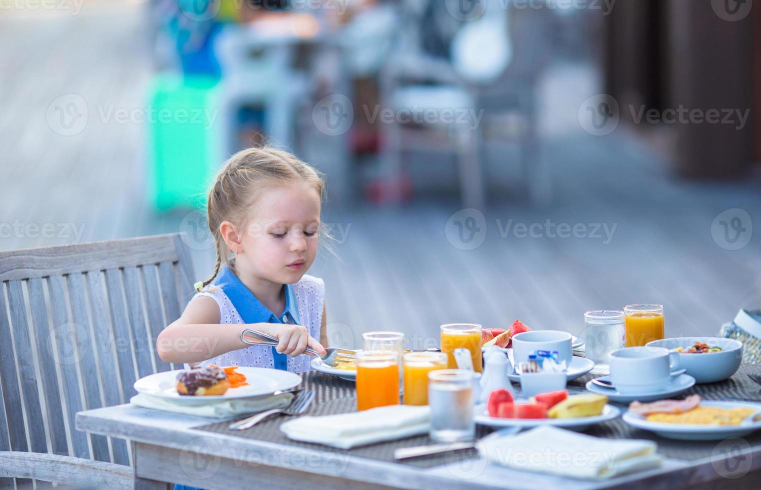 Adorable little girl having breakfast at outdoor cafe photo