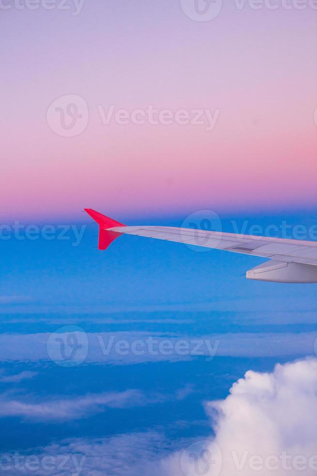 Wing of an airplane flying above the clouds in colorful sky photo