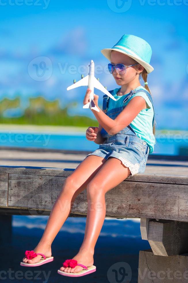 Happy little girl with toy airplane in hands on white sandy beach photo