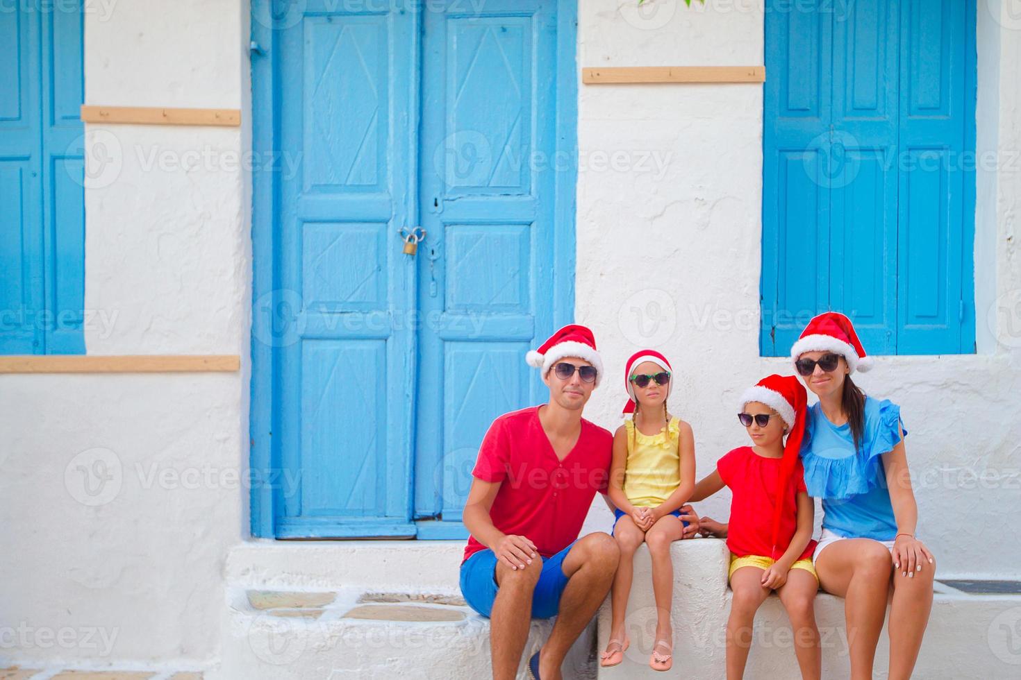 Family in Santa hats on Christmas vacation. Parents and kids at street of typical greek village on Mykonos Island, in Greece photo