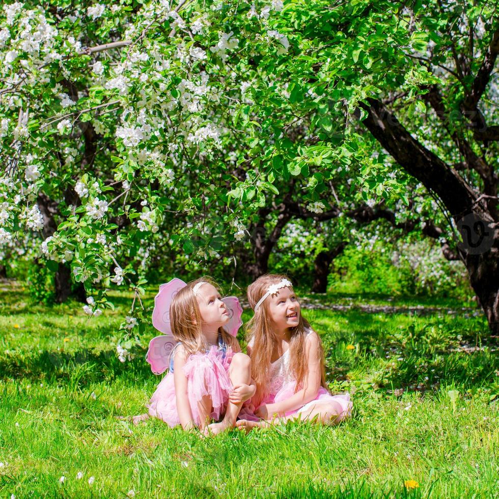 Adorable little girls have fun in blossoming apple tree garden at may photo