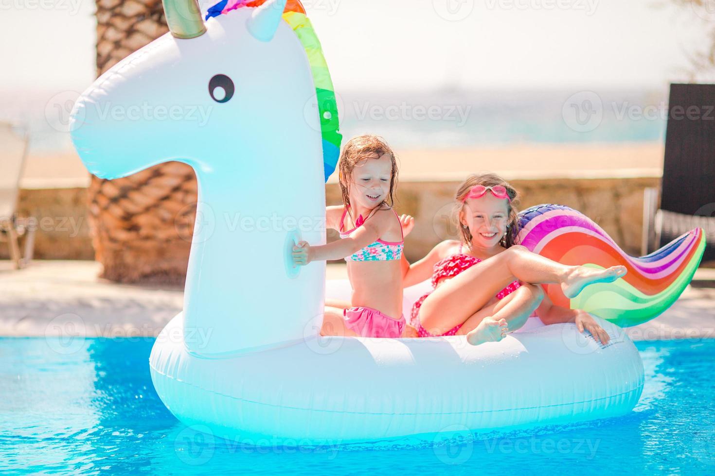 Adorable little girls at swimming pool having fun during summer vacation photo
