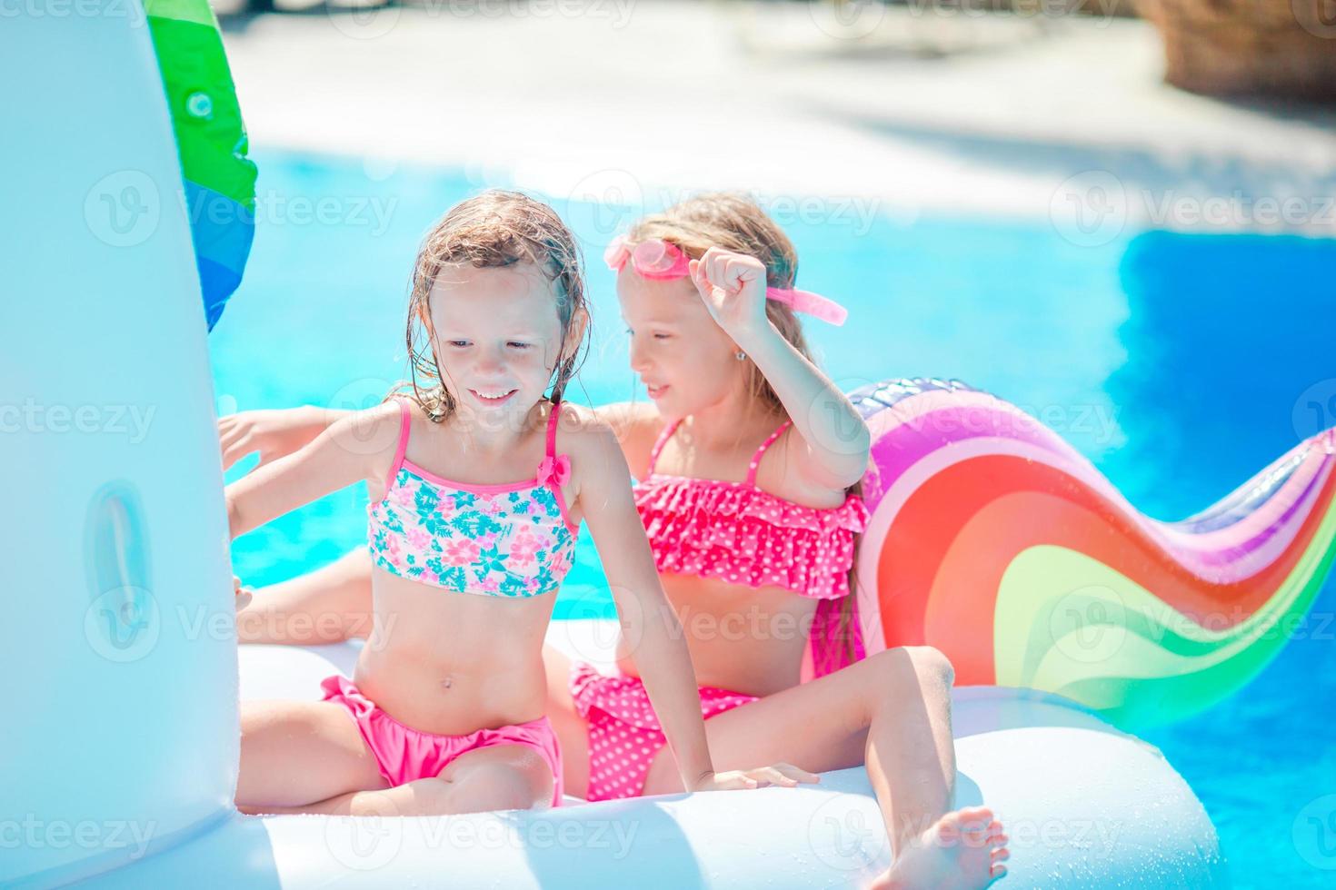 Adorable little girls at swimming pool having fun during summer vacation photo