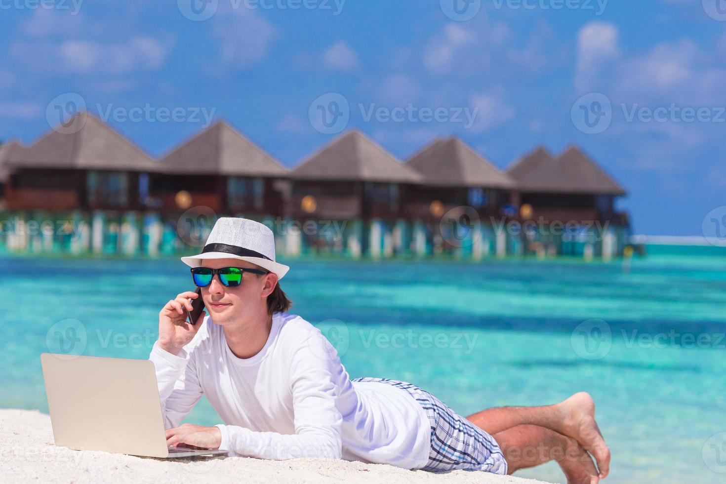 Young man with tablet computer and cell phone on tropical beach photo