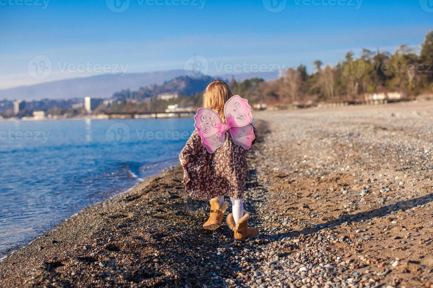 Little girl with butterfly wings running along the beach in a winter sunny day photo