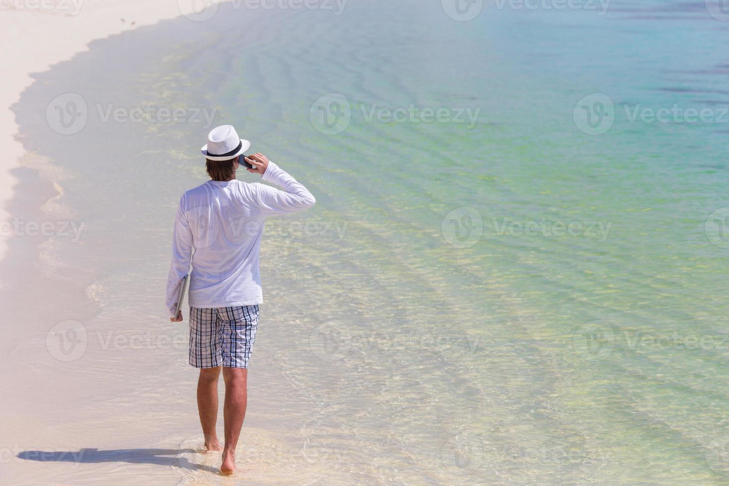Young man talking by cell phone on tropical beach photo