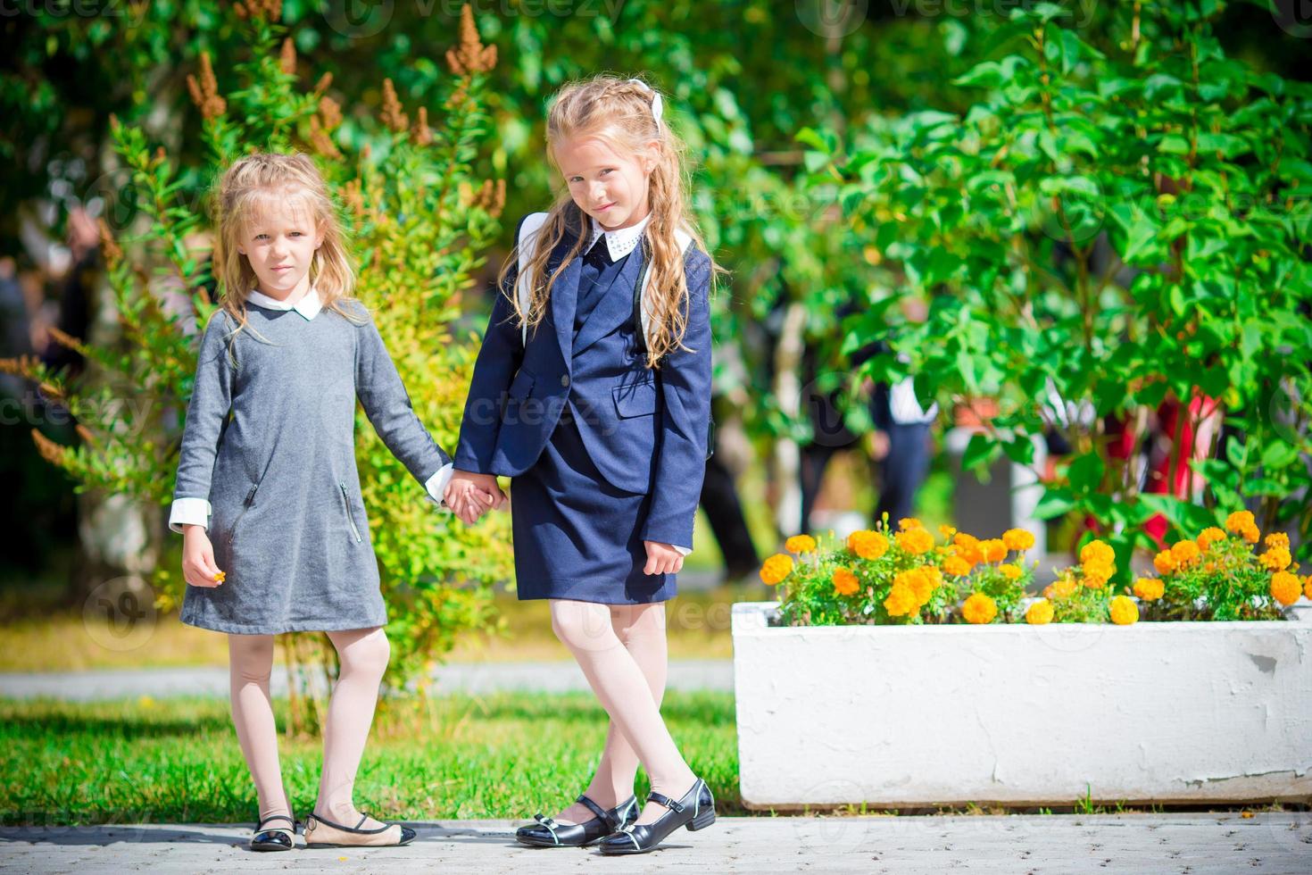 Two cute smilling little girls posing in front of their school. Adorable little kids feeling very excited about going back to school photo