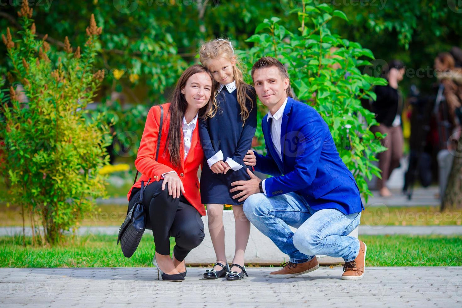 los padres traen a su pequeña y linda hija a la escuela. adorable niña que se siente muy emocionada por volver a la escuela foto