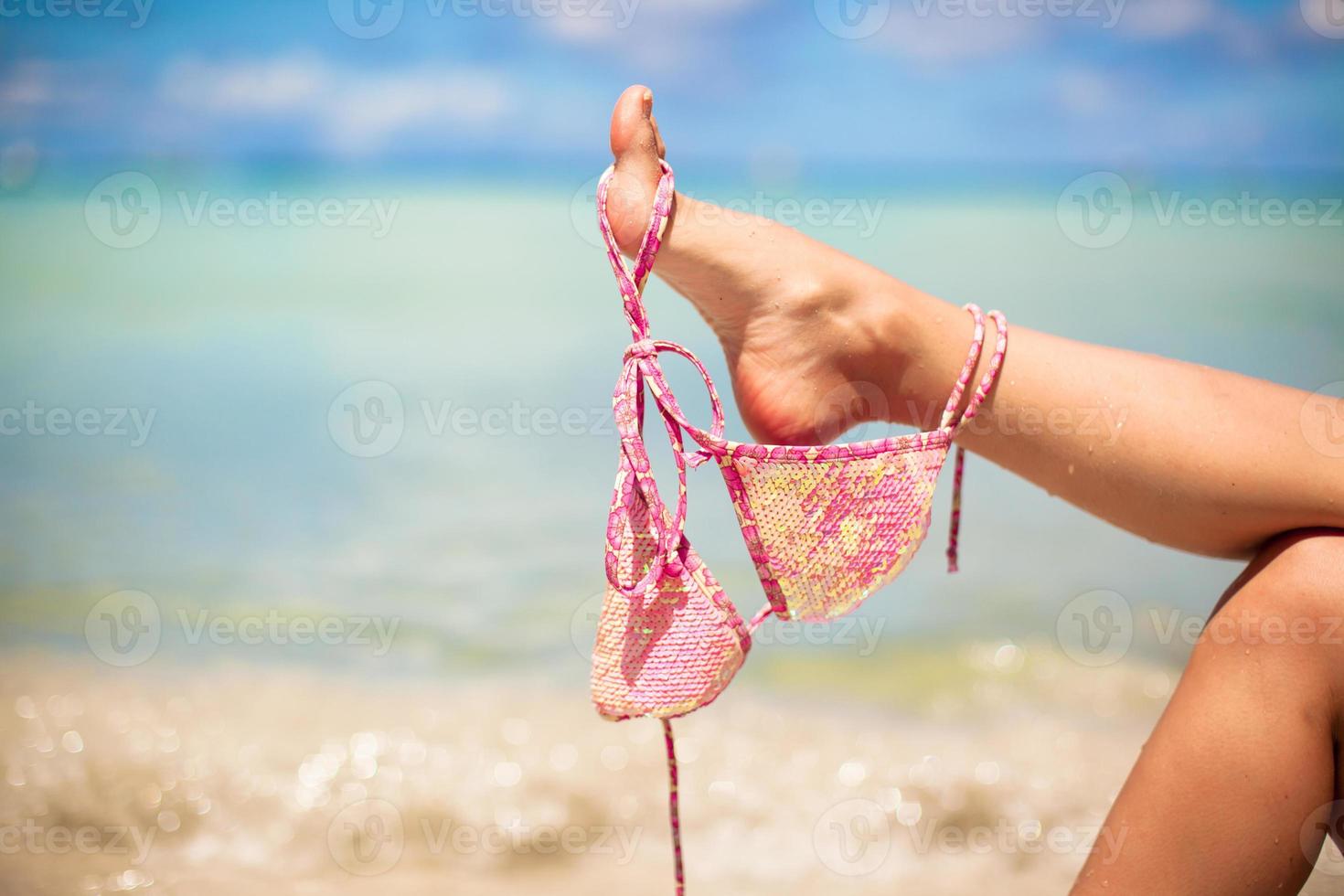 Pink swimsuit on female leg on white tropical beach photo