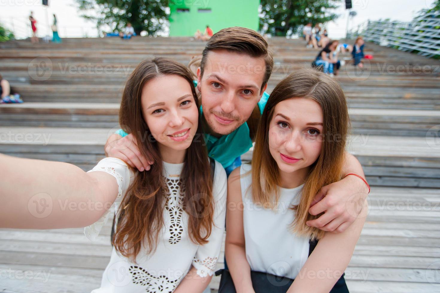 Group of happy teen friends laughing and taking a selfie in the street. Three friends watching taking pictures with tablet pc in park photo