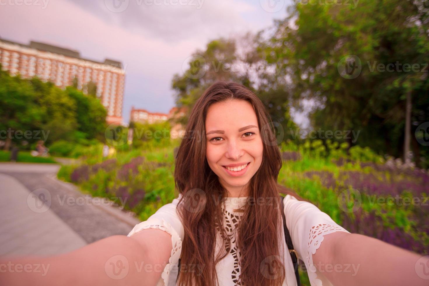 Young caucasian woman making selfie on attractions background outdoors. Happy girl enjoy her weekend in european city photo