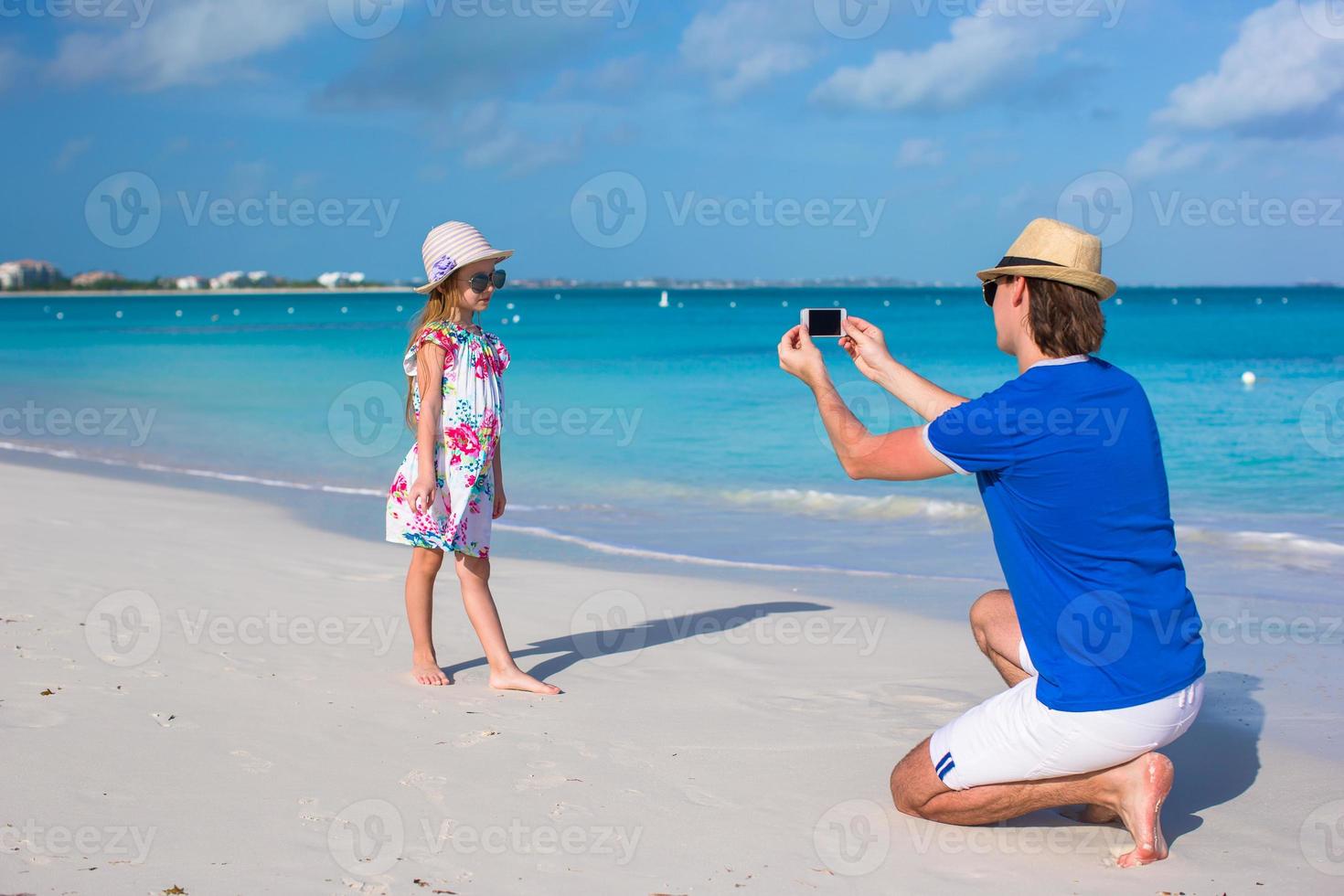 Young father making photo on phone of little girl at beach